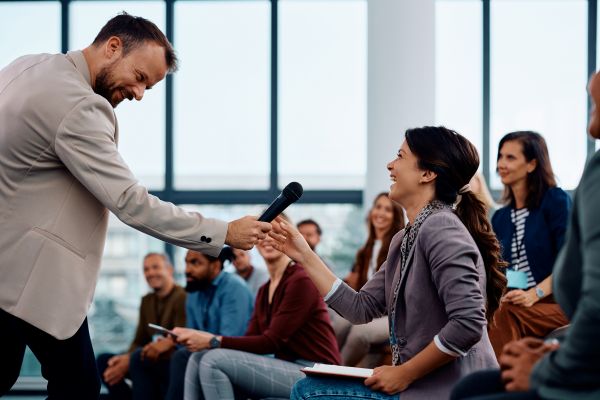 A young man handing a microphone to a young woman at group discussion