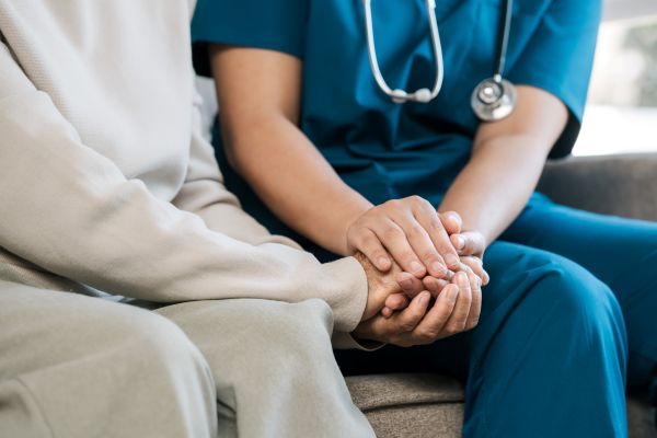 Helpline services - Closeup of a nurse holding a patient's hand while sitting in a hospital