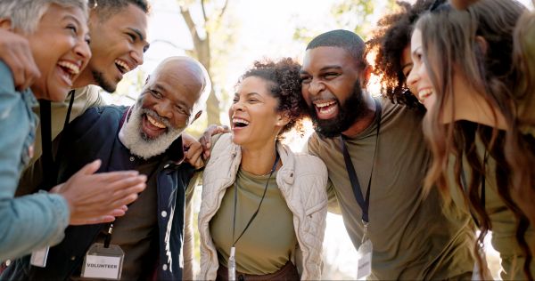 Group of six people smiling and huddling together at a volunteer event, wearing casual clothing and displaying a sense of camaraderie and teamwork.