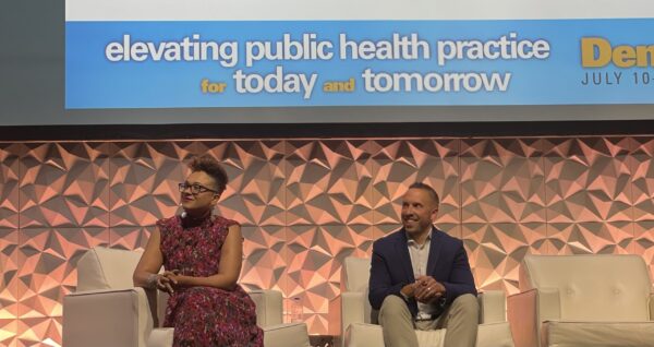 a Black woman and a white man seated on a stage at a convention center